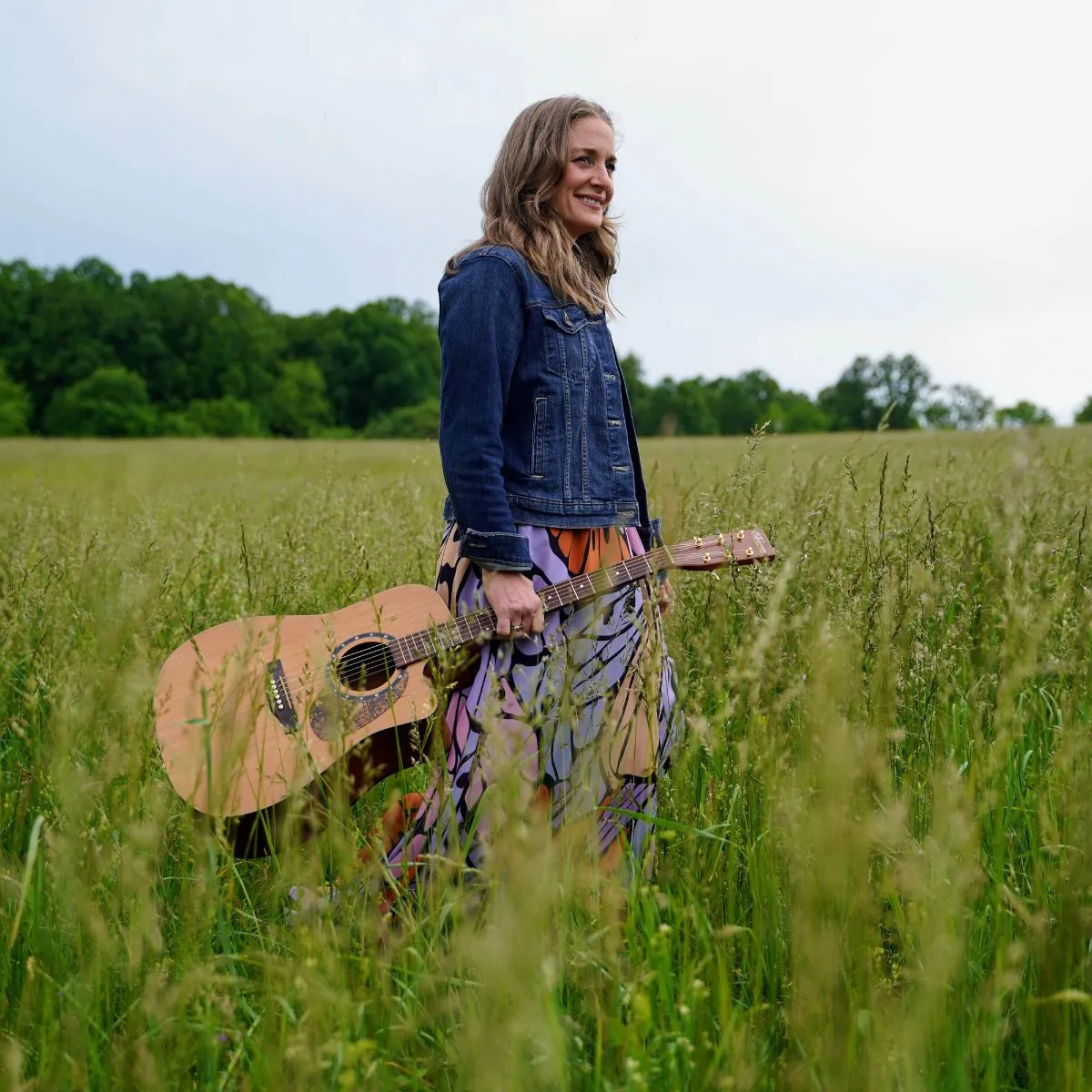Liz Watkins of Liz Watkins music standing in a field with a guitar